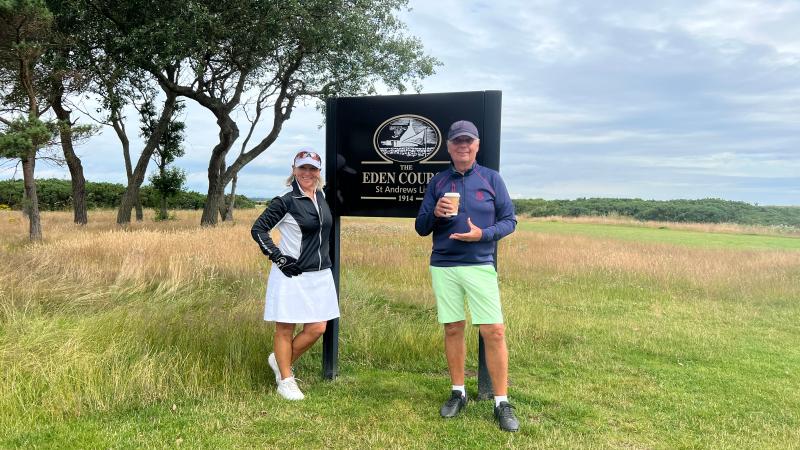 Två golfare står vid skylten till The Eden Course i St Andrews med gräsfält och träd i bakgrunden.